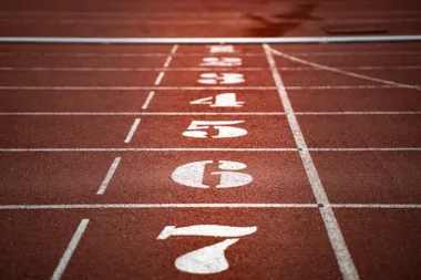 Widok torów lekkoatletycznych z czerwonym tartanem i białymi numerami 7–1 namalowanymi w perspektywie