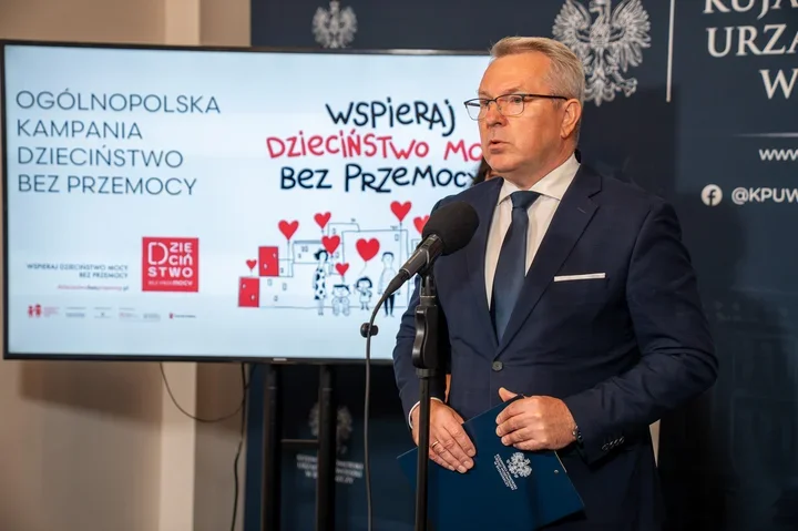 Mężczyzna w garniturze przemawia do mikrofonu podczas konferencji prasowej ogólnopolskiej kampanii „Dzieciństwo bez przemocy”.