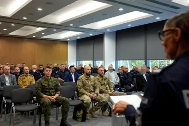 Funkcjonariusz służb mundurowych przemawia do grupy oficerów i przedstawicieli służb w sali konferencyjnej.