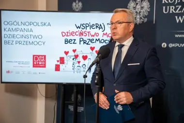 Mężczyzna w garniturze przemawia do mikrofonu podczas konferencji prasowej ogólnopolskiej kampanii „Dzieciństwo bez przemocy”.