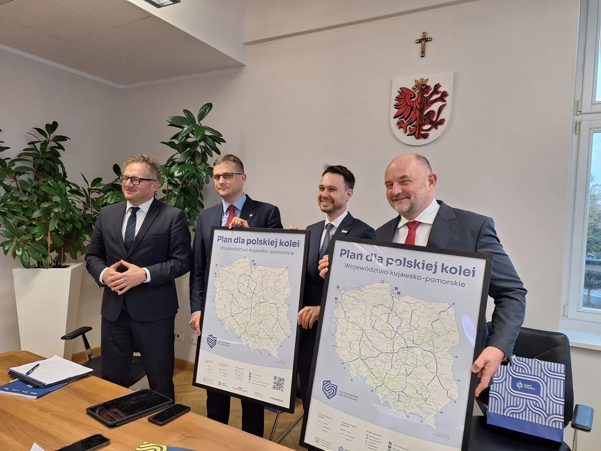 Czterej mężczyźni w garniturach prezentują w urzędowej sali plany kolejowe dla województwa kujawsko-pomorskiego.